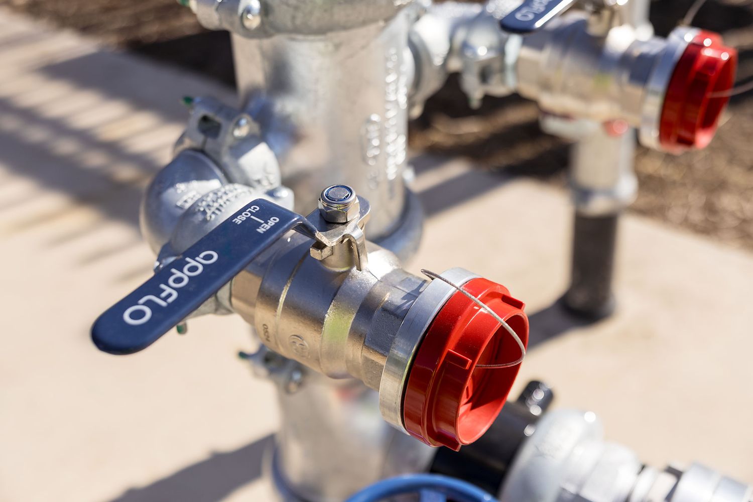 Close-up of an OppFlo industrial pipe valve with red cap fitting on outdoor piping system.