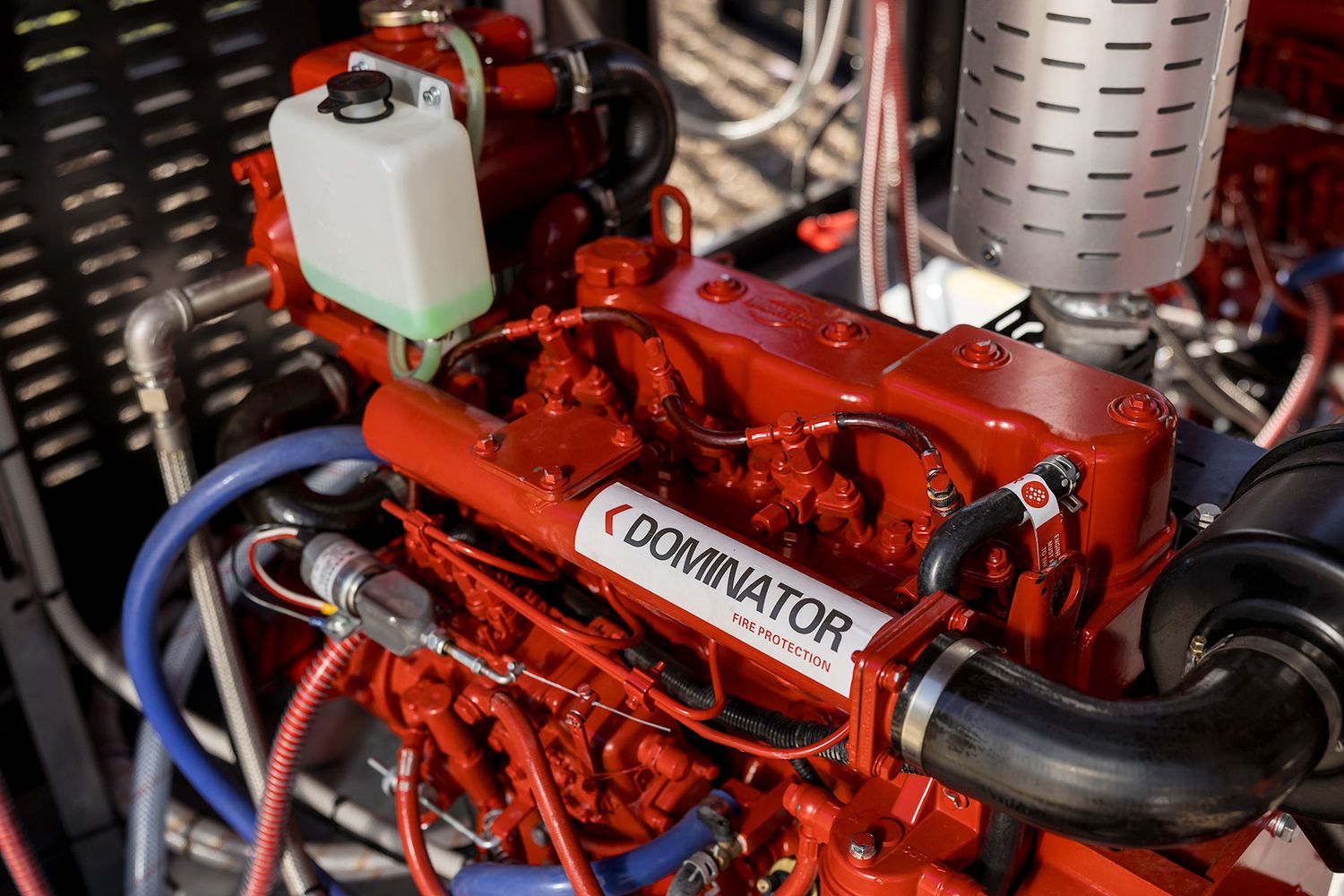 Close-up of a red Dominator marine engine with blue hoses and components in an engine compartment.