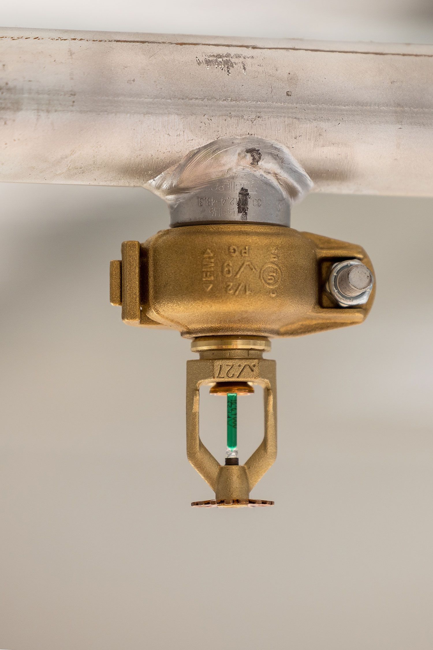 Close-up of a brass fire sprinkler head mounted on a ceiling pipe for fire suppression systems.