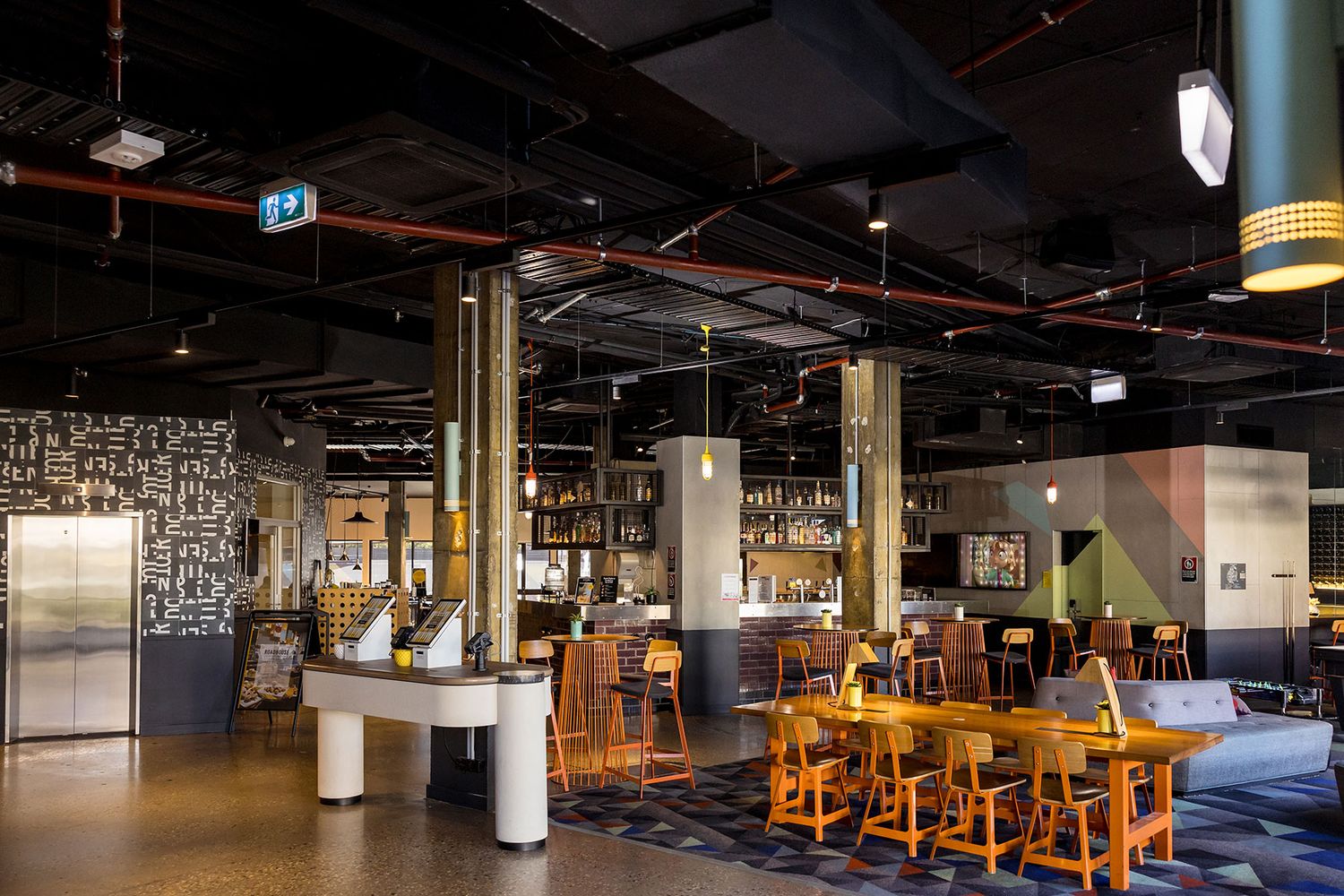 Modern industrial bar lounge at Atura in Albury with exposed black ceiling, pool table, pendant lights, and colorful geometric wall accents.