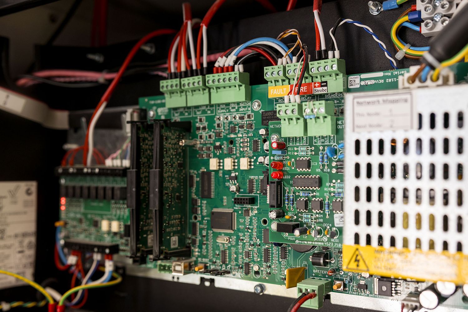 Close-up of a green circuit board with wiring and electronic components inside an industrial control panel.