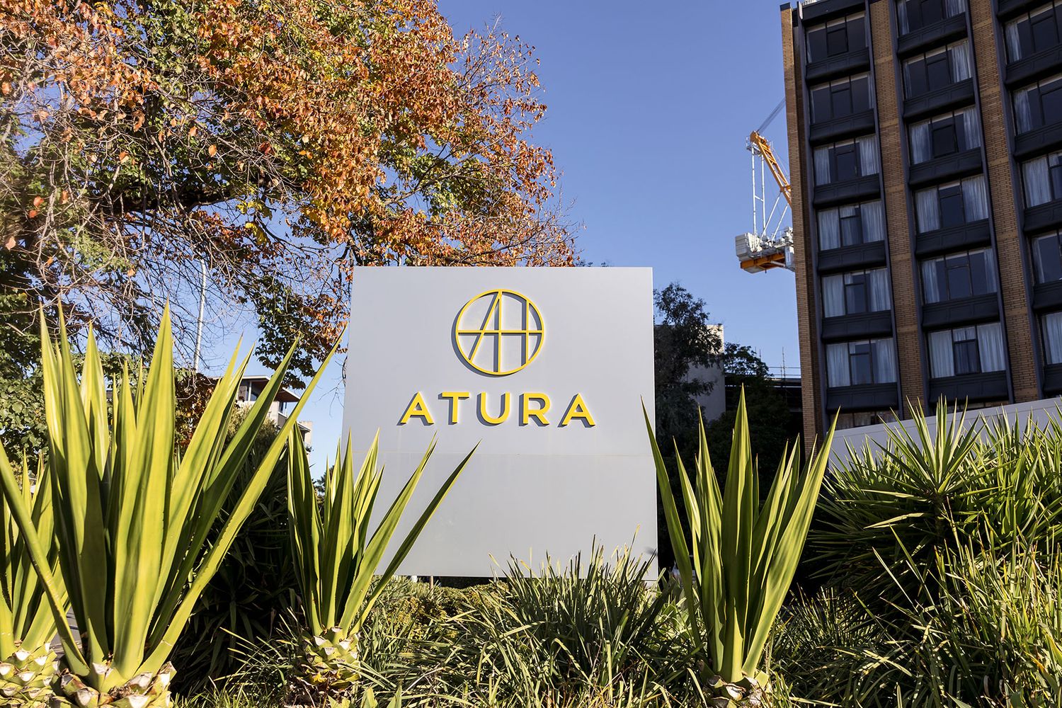 Atura hotel sign in Albury with golden logo surrounded by lush greenery and modern building in background.