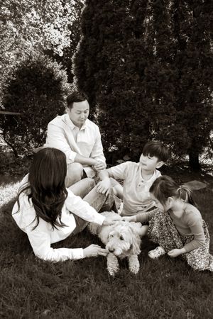 Black and white photo of a family with two children and a fluffy dog sitting together on grass in a garden.