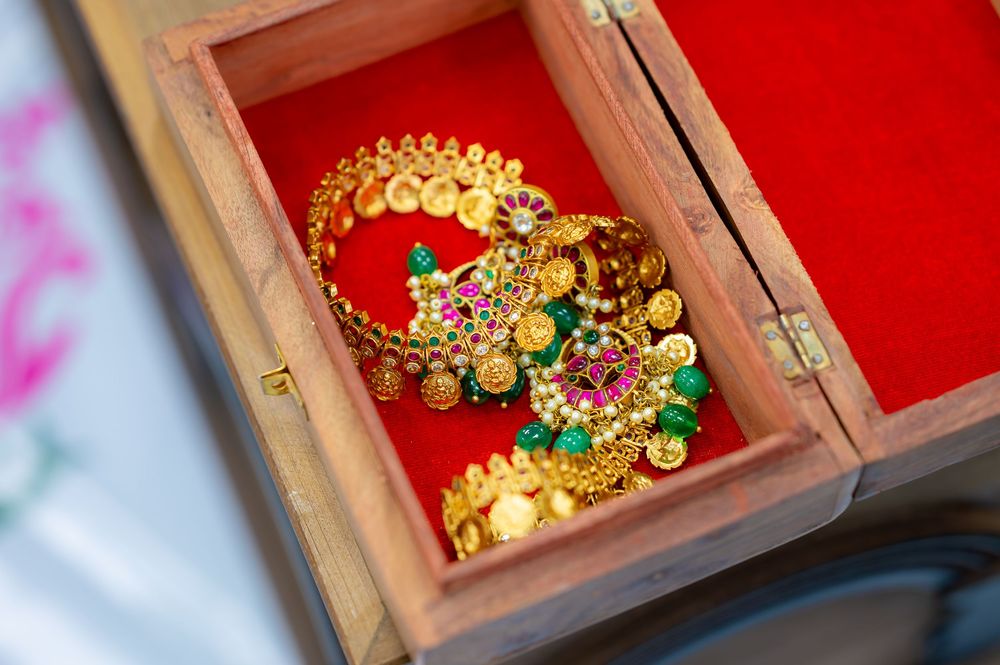 Gold Indian bridal bangles with ruby and emerald gemstones displayed in a wooden box with red velvet lining.