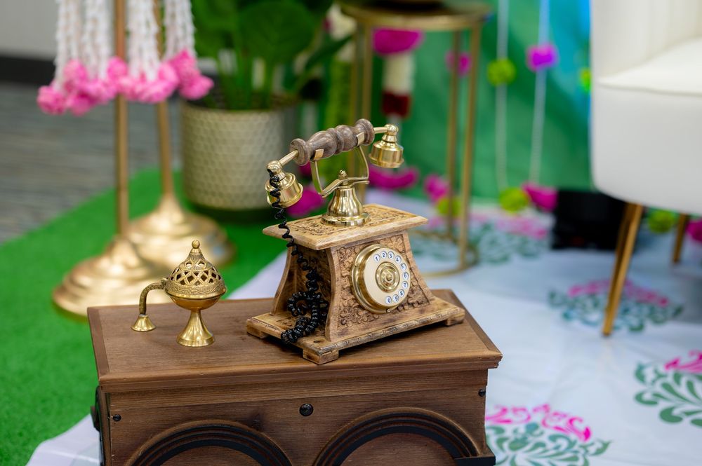 Ornate vintage brass telephone on a decorative wooden box with colorful floral decor in the background.