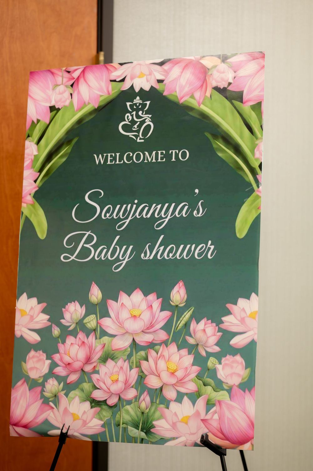 Welcome sign for Sowjanya's Baby Shower decorated with pink lotus flowers on a green background.