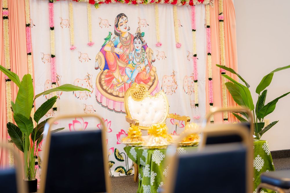 Hindu deity Radha Krishna painting displayed on decorated altar with floral backdrop at traditional Indian ceremony.
