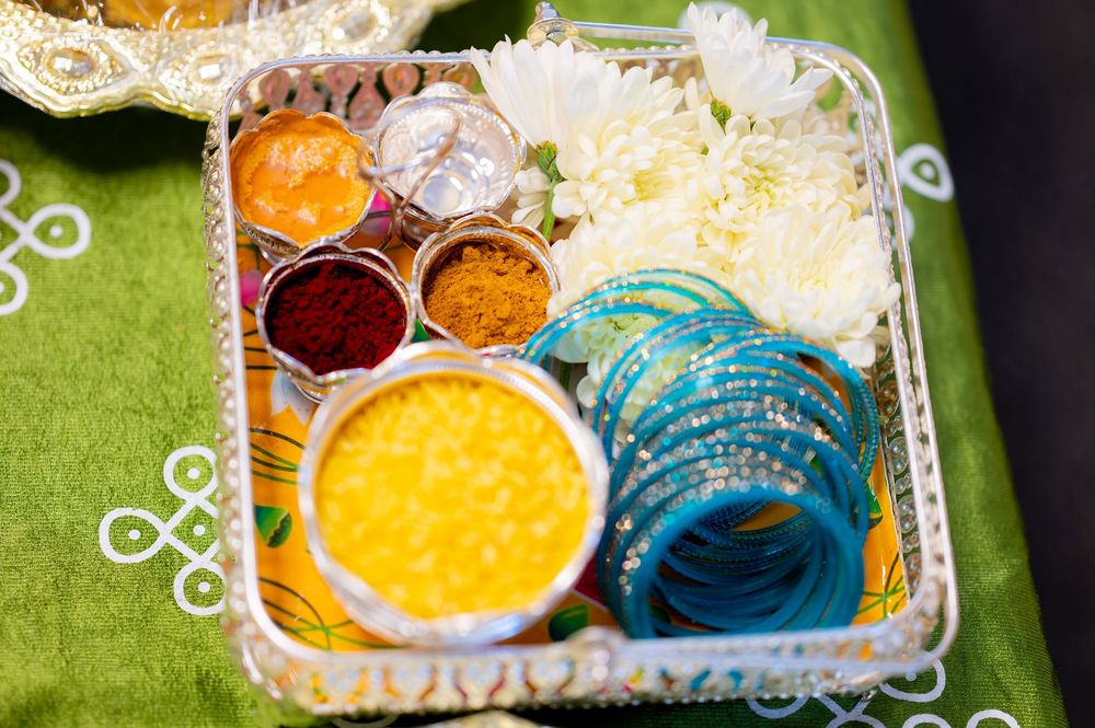 Indian Haldi ceremony tray with colorful spices, white flowers, and blue bangles on green fabric.