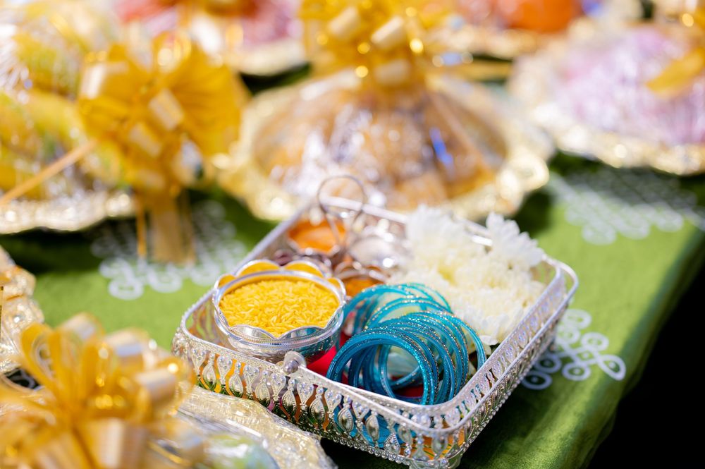 Colorful traditional Indian wedding gift trays with bangles, turmeric, and decorative yellow bows on green cloth.