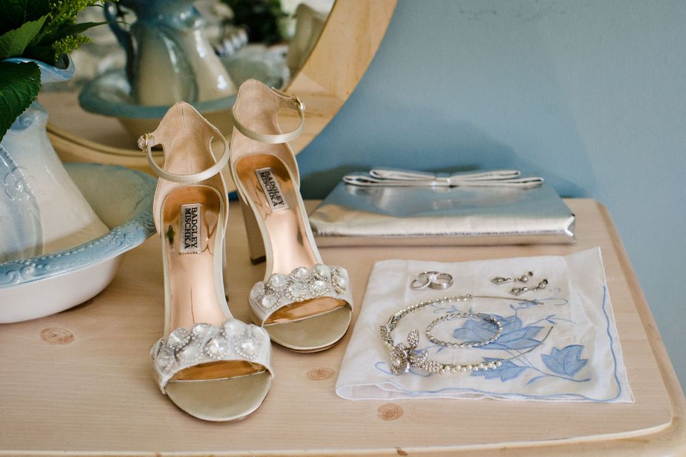 Elegant bridal accessories including embellished heels, pearl jewelry, and a decorative handkerchief on a wooden dresser.