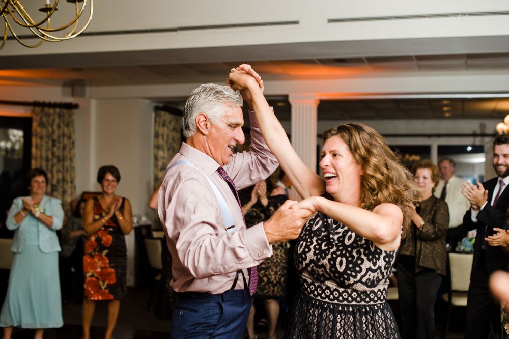 Joyful couple dancing together at a wedding reception while guests clap and celebrate in the background.
