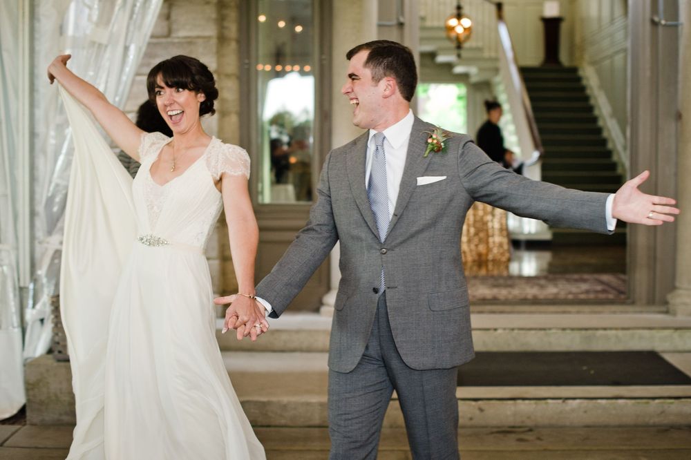 Joyful bride in white gown and groom in gray suit celebrating their wedding entrance with arms outstretched.
