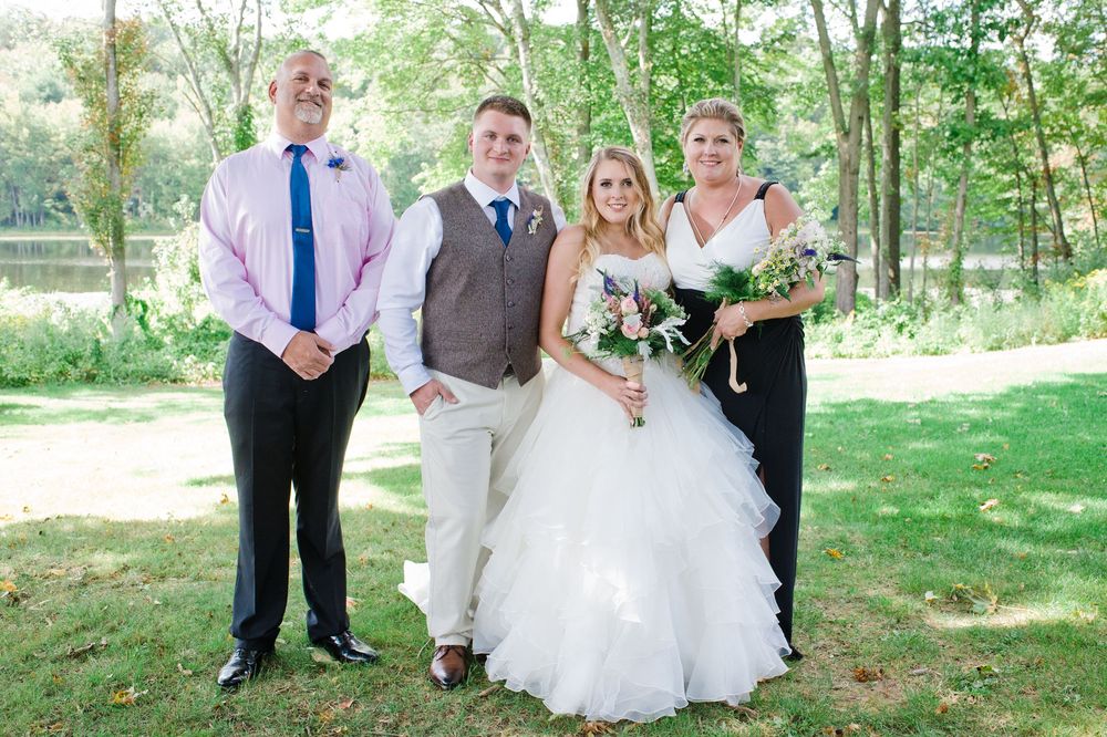 Wedding party of four posing outdoors in a wooded setting, bride in ruffled white ballgown with bouquet.