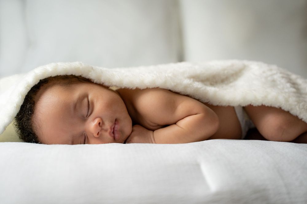 Peaceful newborn baby sleeping under a soft white blanket on a white surface.