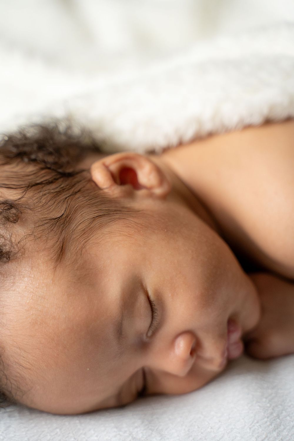 Peaceful newborn baby sleeping on a white fluffy blanket, close-up portrait of an infant with curly hair.