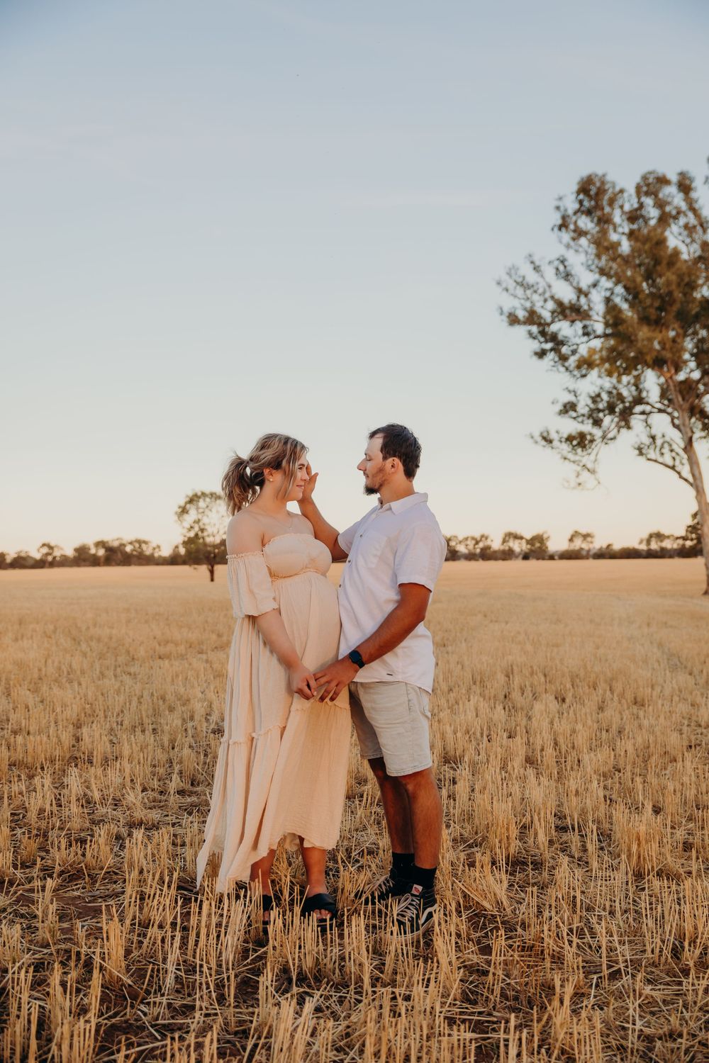 Expecting couple holding hands and gazing at each other in a sun-drenched wheat field.