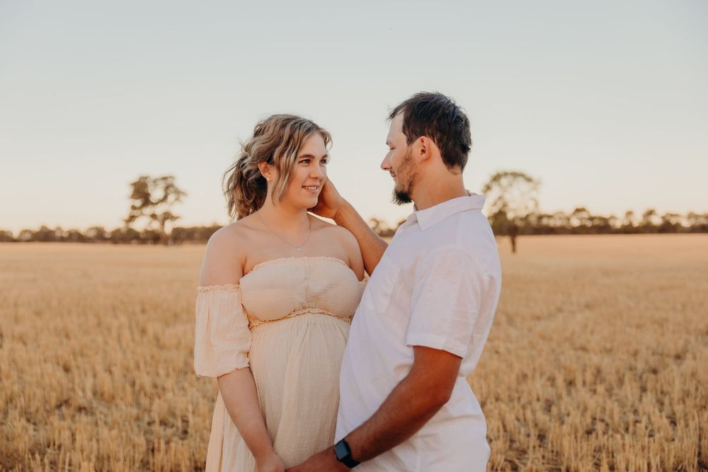 Happy pregnant couple sharing a tender moment in a golden wheat field at sunset.
