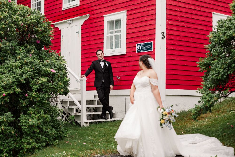 Bride and groom walk hand-in-hand outside a charming red building on their wedding day.