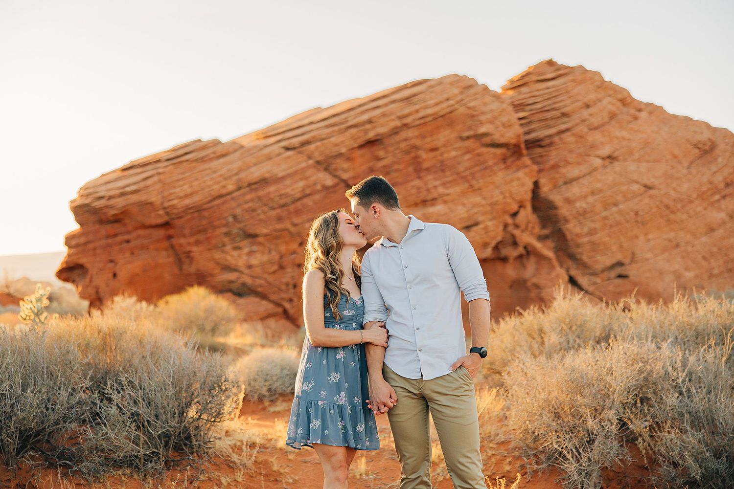 Couple kissing in desert landscape with red rock formations and golden hour light at Red Rocks Park.