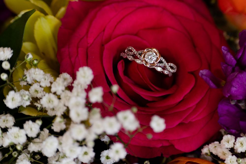 Diamond engagement ring resting in a vibrant red rose with white flowers.