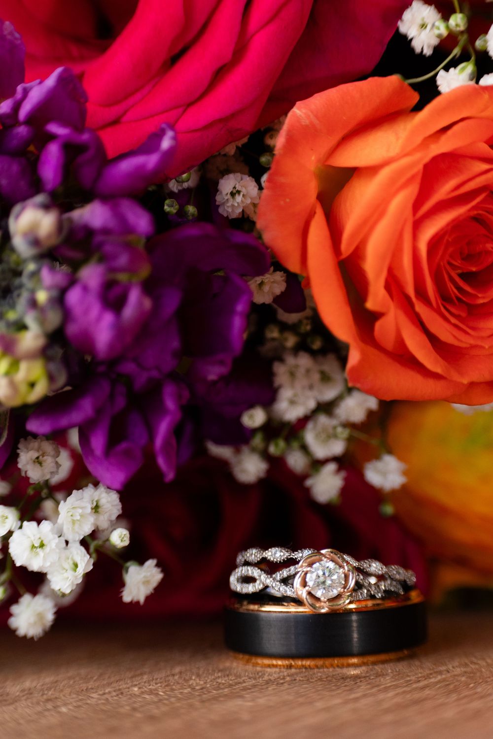 Wedding rings displayed in front of a vibrant bouquet of orange, pink, and purple roses.