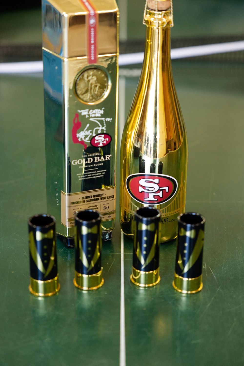 San Francisco 49ers gold bar whiskey bottle with shot glasses on a green surface.