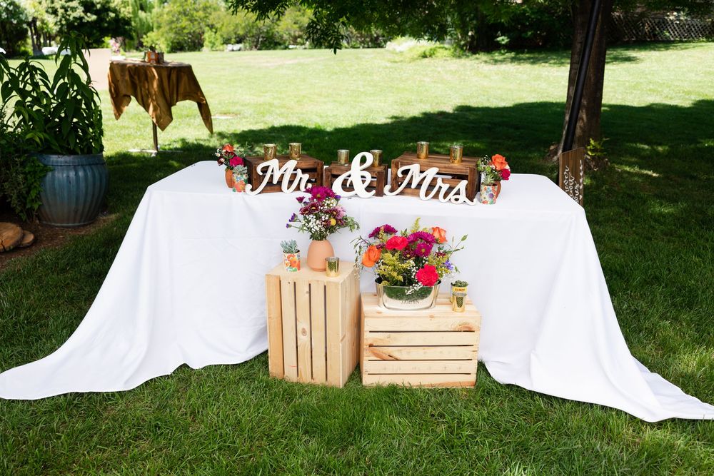An outdoor Mr. and Mrs. sweetheart table decorated with wooden crates and colorful floral arrangements on green grass.