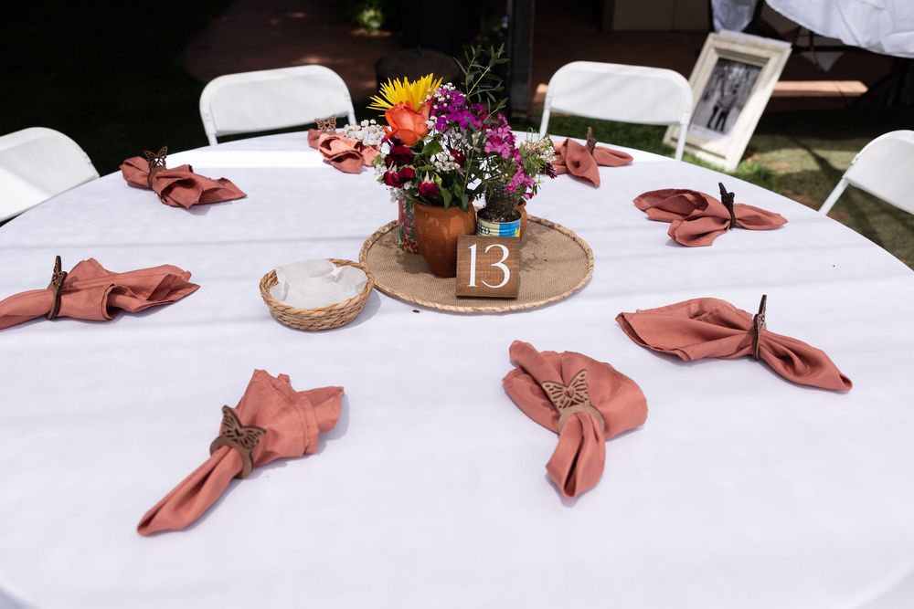 Wedding reception table set with terracotta napkins, wildflower centerpiece, and table number 13 on wood slice.
