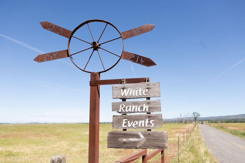 Rustic White Ranch Events venue sign with wagon wheel decoration under a clear blue sky.