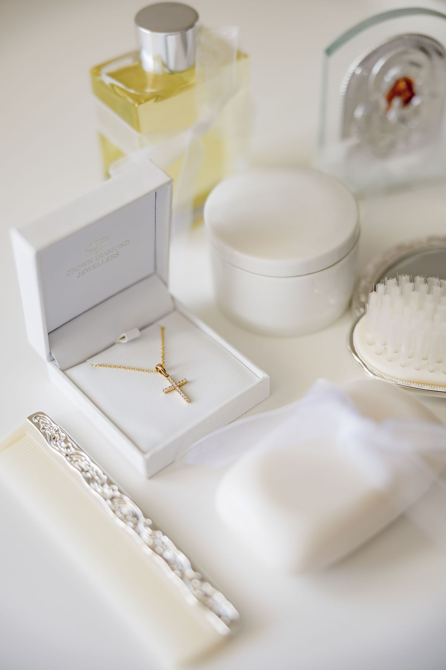 Gold cross necklace in white jewelry box with perfume, brush, and white candle for baptism ceremony.