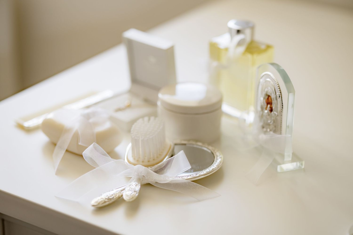 Elegant white christening accessories arranged on a table including brush, mirror, cream jar, and religious figurine.