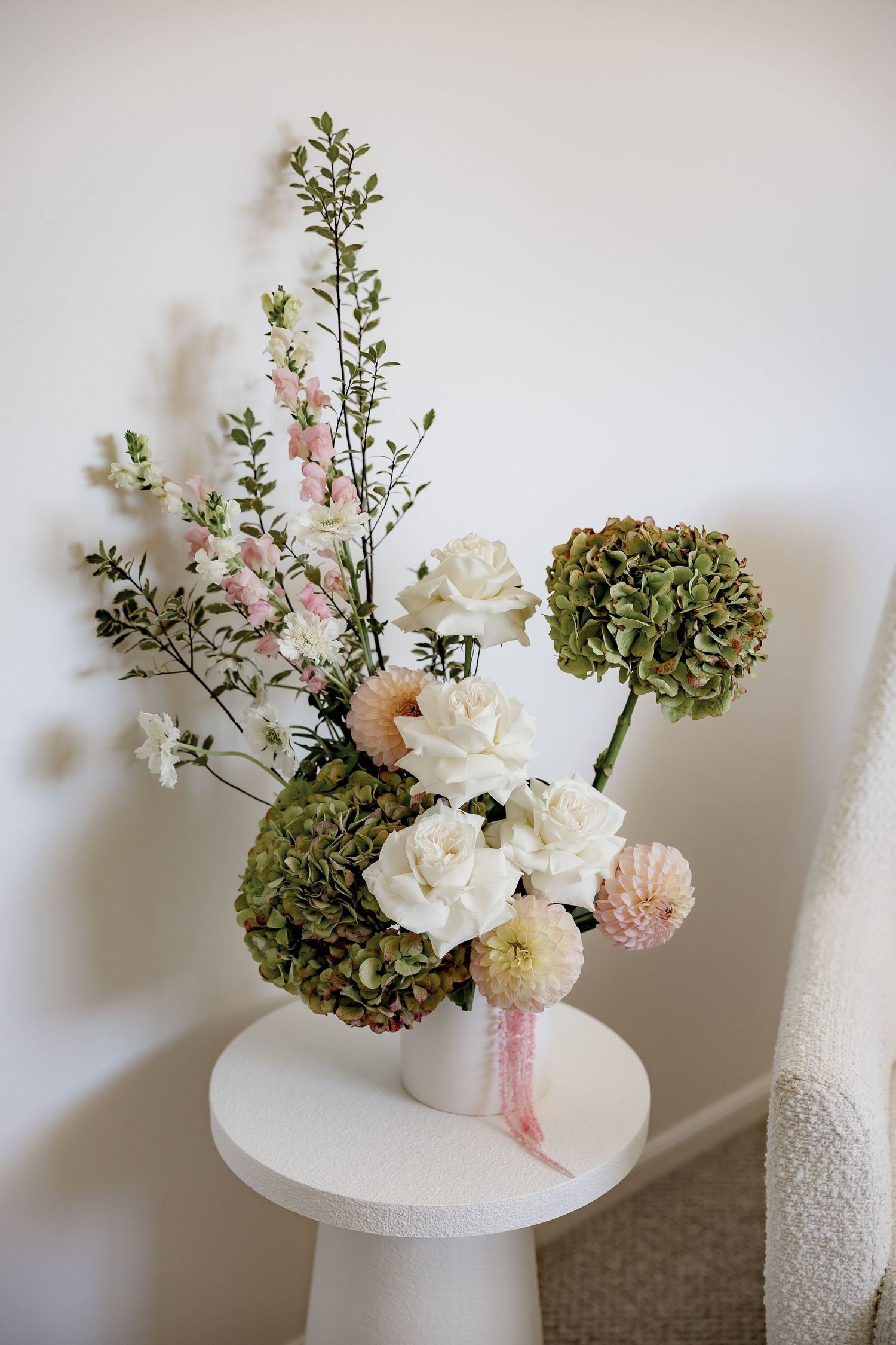 Elegant floral arrangement with white roses, green hydrangeas, and pink blooms in a white vase on a small round table.
