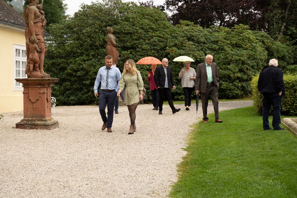 Wedding guests walking along a gravel path past stone statues in a formal garden.