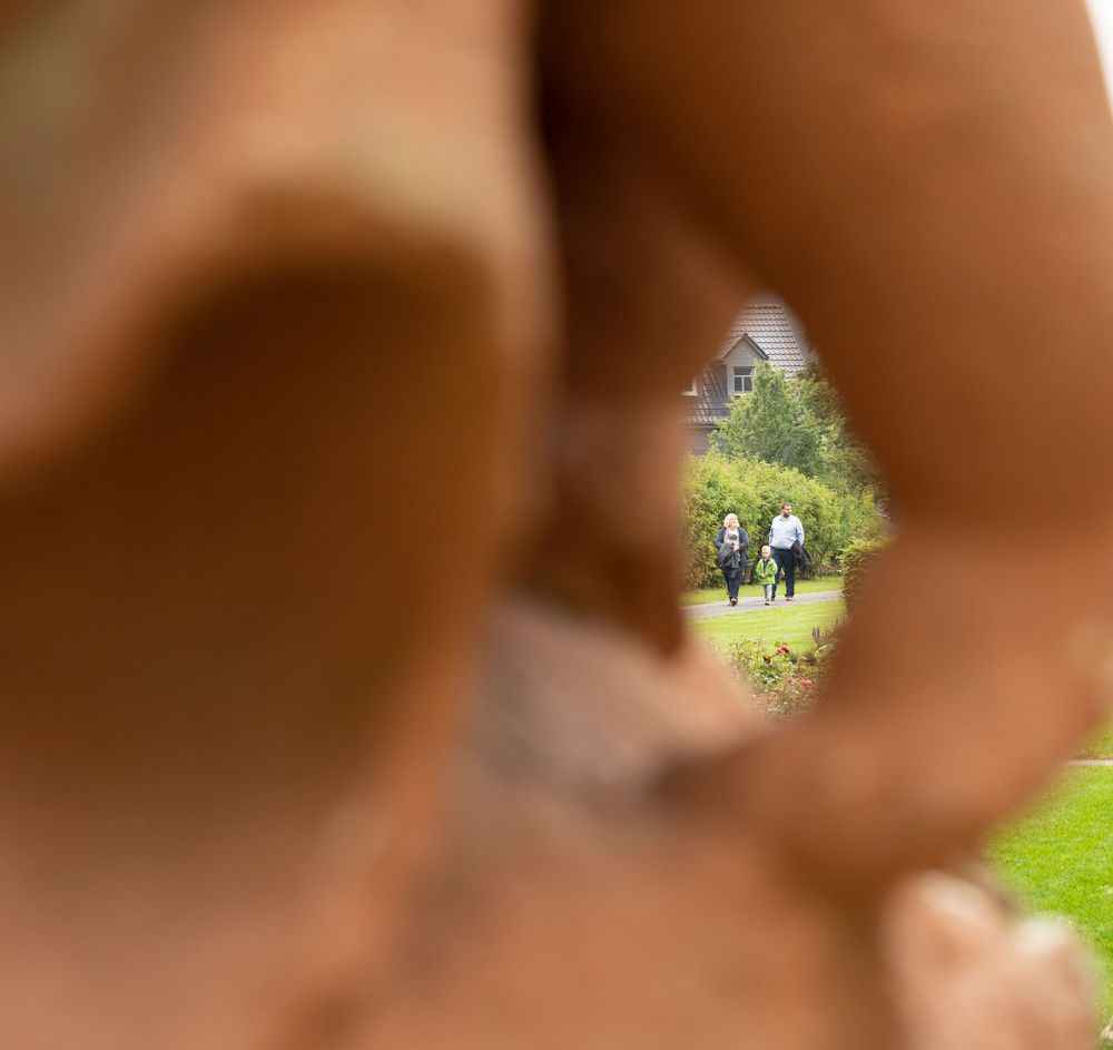 Two people walking in a garden viewed through a hole in a rustic stone sculpture.