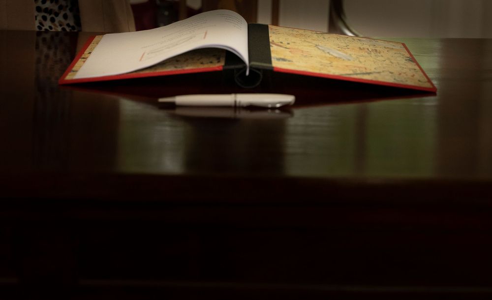 An open wedding guest book with a pen resting on a dark wooden table in soft lighting.