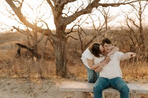 Couple embracing on a wooden bench at golden hour with bare trees in a rustic outdoor setting.