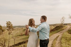 Couple dancing together on a scenic hilltop dirt road surrounded by lush green countryside.