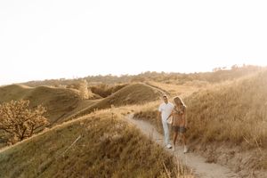 Couple walking hand in hand on a scenic golden hill path during sunset.