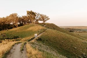 Couple walking along a winding path on rolling green hills at golden hour sunset.