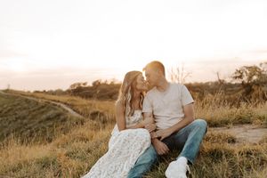 Couple sharing a romantic kiss at sunset in a golden field, sitting together in a warm outdoor setting.