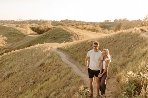 Couple walking hand in hand on a scenic dirt path through golden hills at sunset.