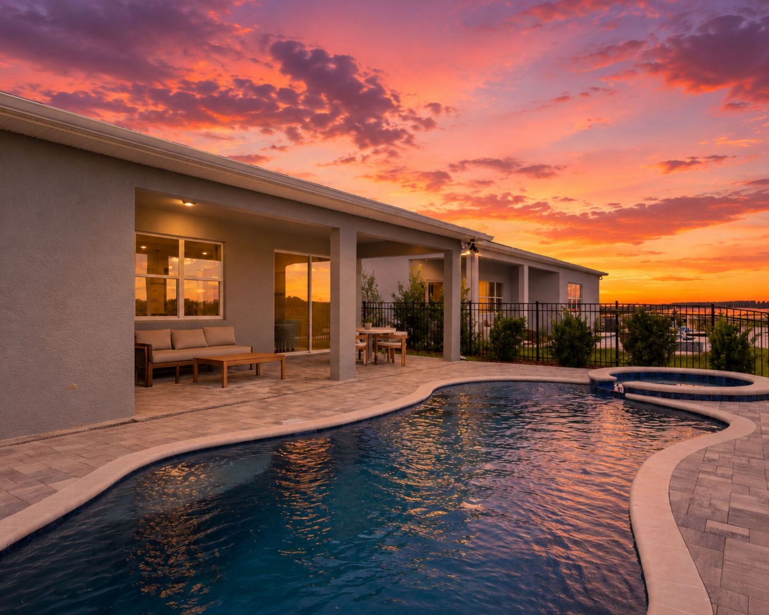 Luxury backyard pool with spa at sunset, featuring a stunning orange and pink sky behind a modern home.