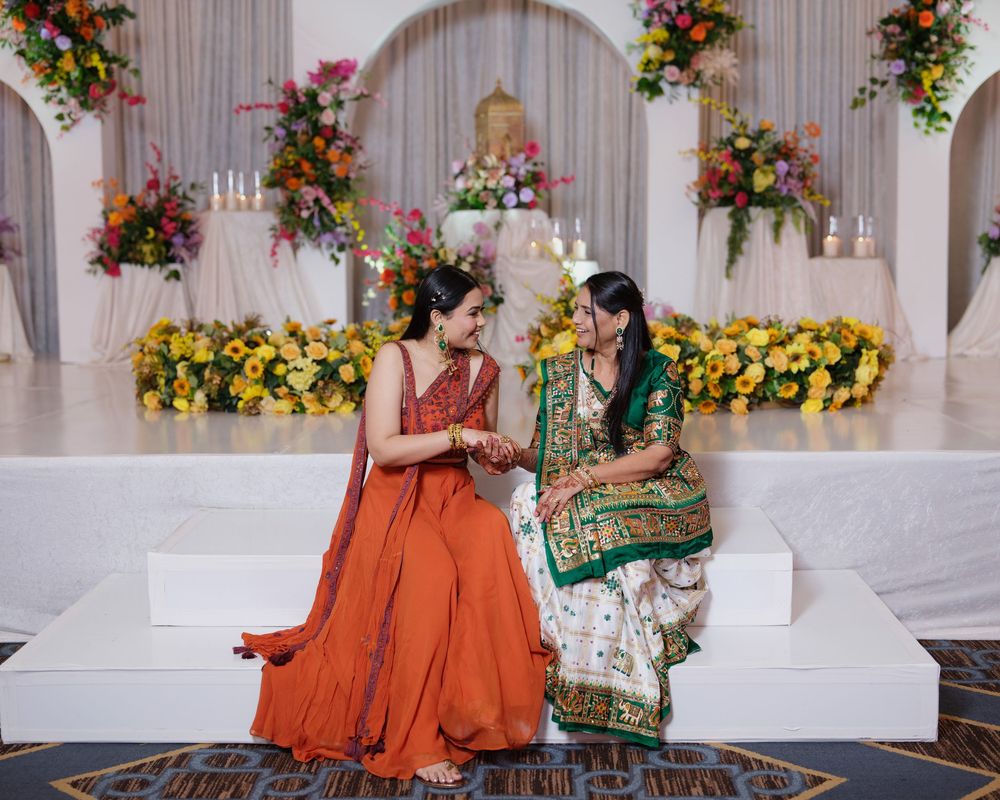 Two women in vibrant Indian attire share a joyful moment at a decorated wedding ceremony venue.