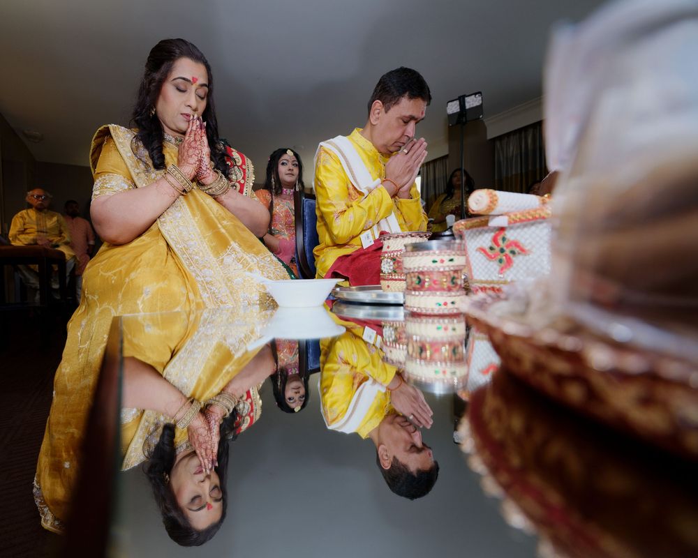 Couple in golden attire praying at Indian wedding ceremony with reflection on polished table surface.