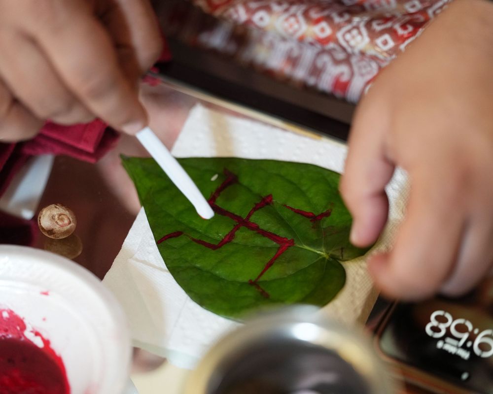 Child painting red designs on a green leaf using a cotton swab as a brush.
