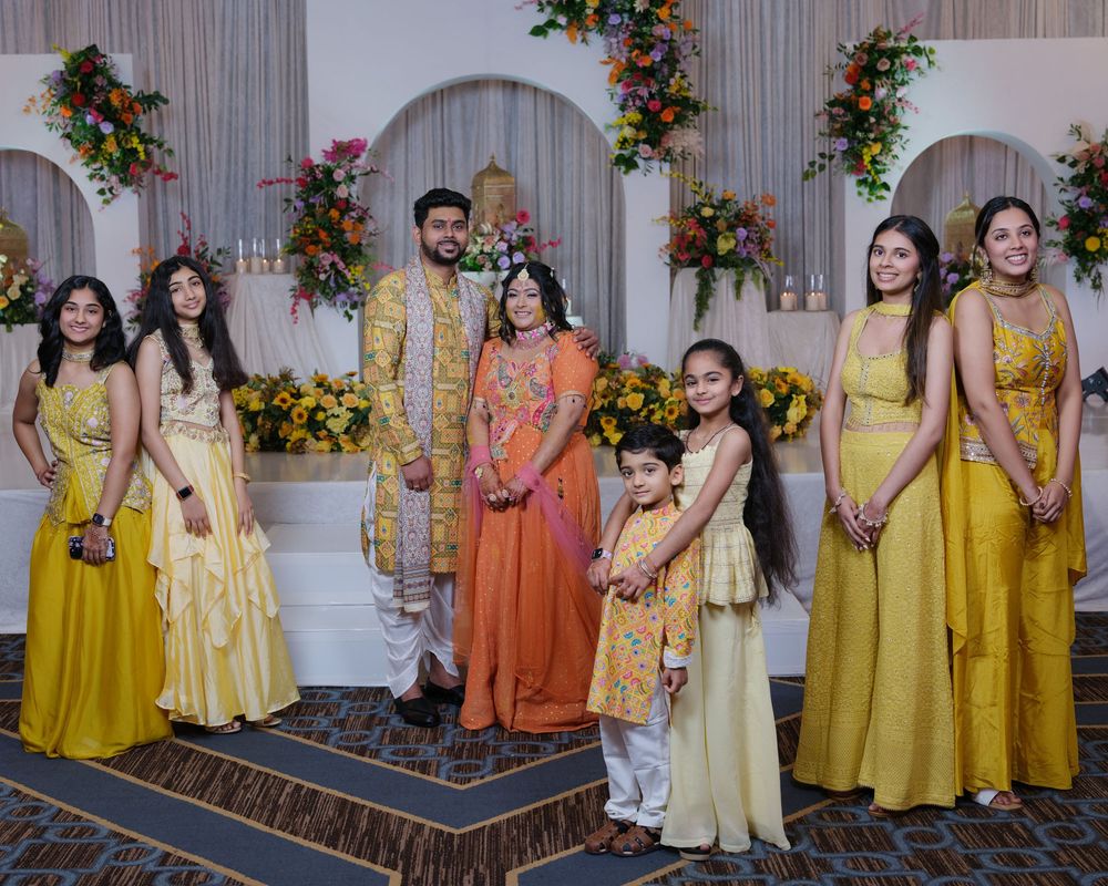 Family group photo in coordinating yellow outfits at a vibrant Indian wedding celebration.