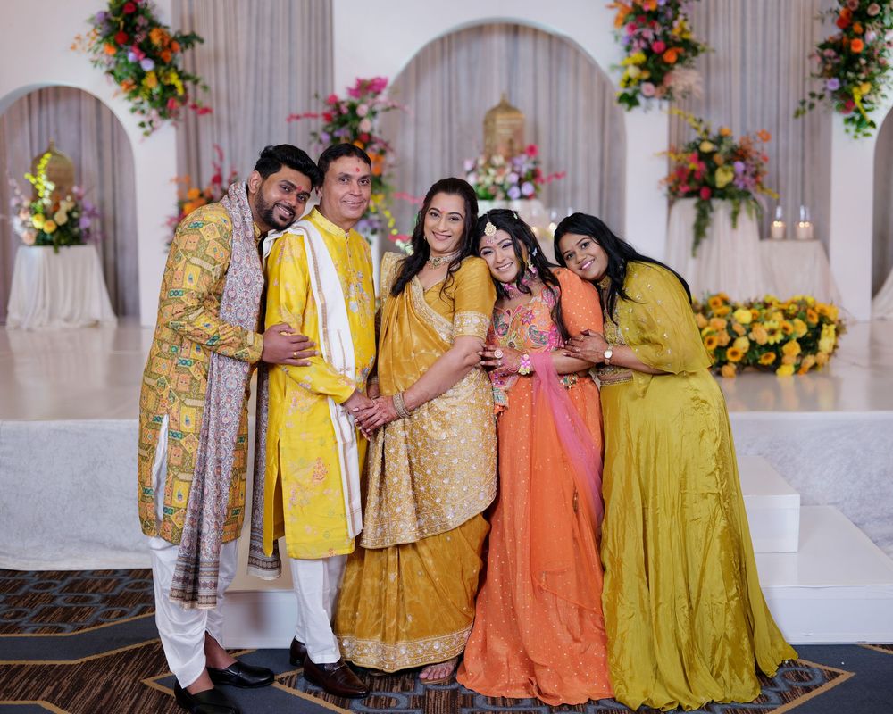 Five people in vibrant yellow and orange Indian attire pose together at a festive wedding celebration.