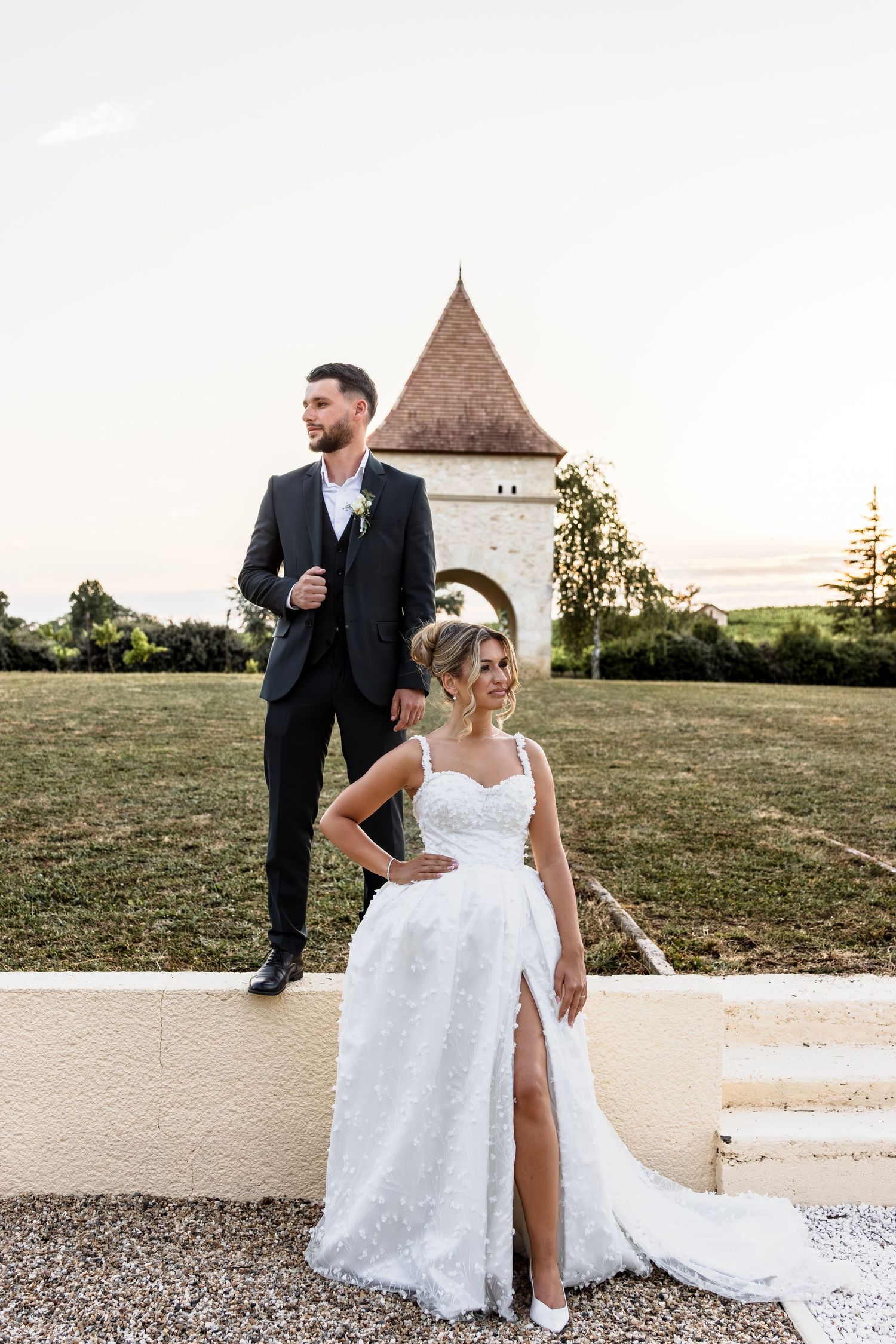 A bride and groom share a romantic moment outdoors, she in a floral gown, he in a dark suit with boutonniere.