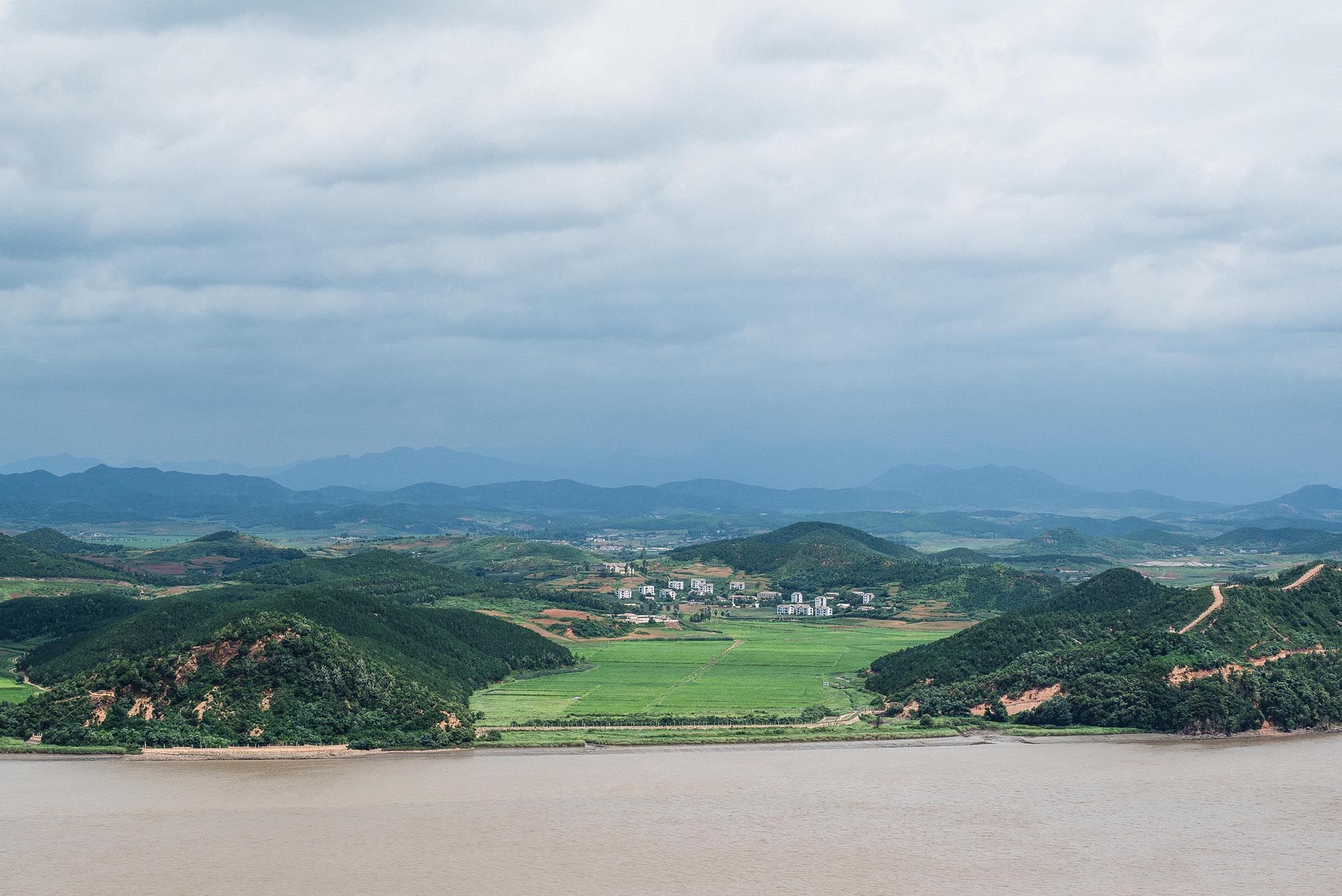 Aerial view of a lush green valley with a river, small town, and mountains under cloudy skies in Vietnam.