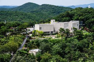 Aerial view of a modern museum building nestled among lush green forested hills in South Korea.